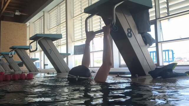 Adult woman performs aquatic rehabilitation pull up exercises in an indoor swimming pool, improving upper body strength, mobility, recovery, balance, and functional fitness safely