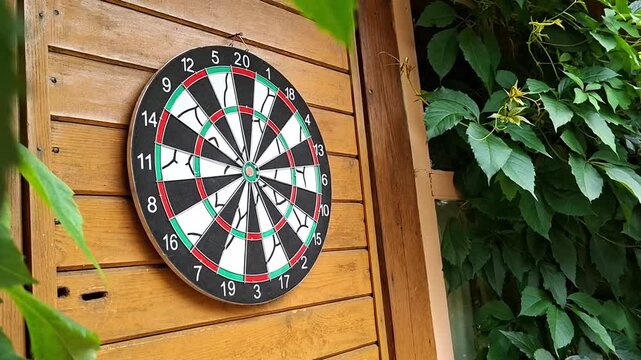 Dart hitting target board hanging on wooden wall. Player throwing arrow during game on holiday.