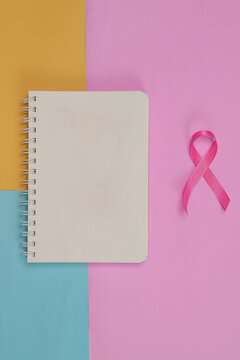 Breast cancer awareness concept with pink ribbon and notepad on colorful background