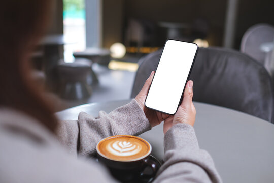 Mockup image of a woman holding mobile phone with blank desktop screen in cafe