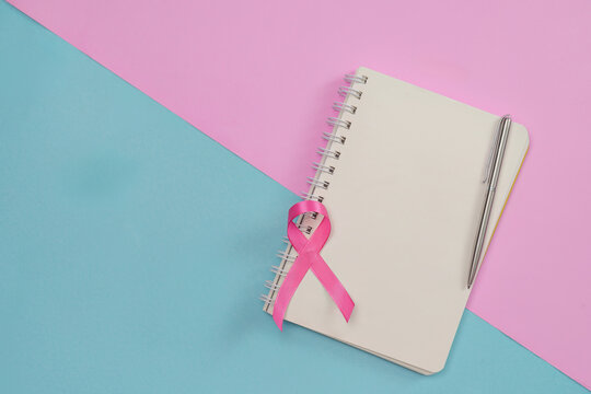 Breast cancer awareness concept with pink ribbon notebook and pen on pink blue background