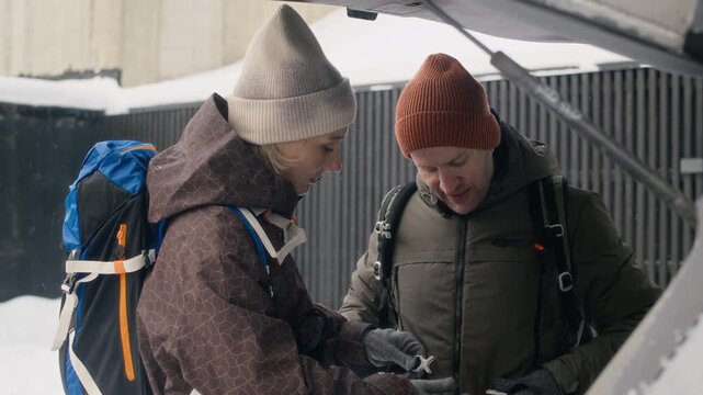 Caucasian adult woman helping Caucasian middle aged man adjust backpack straps during winter outdoor trip. Perfect for travel gear commercials and active lifestyle marketing