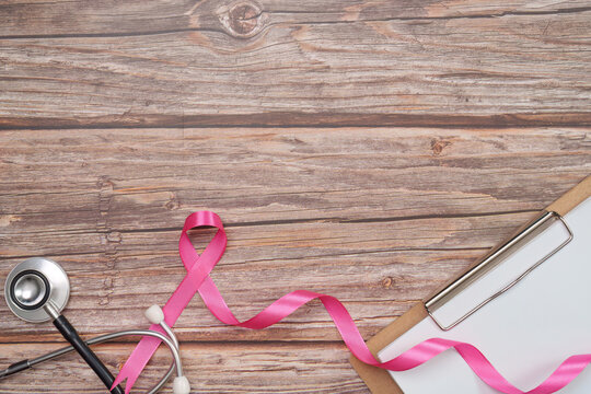 Breast cancer awareness concept with stethoscope clipboard and pink ribbon on wood background
