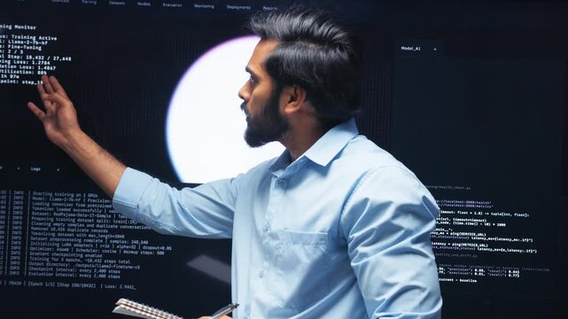 Professional Indian Software Developer, AI Engineer looking at Screen Reviewing and Analyzing Data, AI Model and Coding while Taking notes and Information report Standing in Control room at Office.