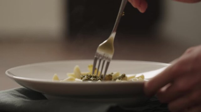 Slow motion making pesto penne pasta with mozzarella and tomatoes in deep plate closeup