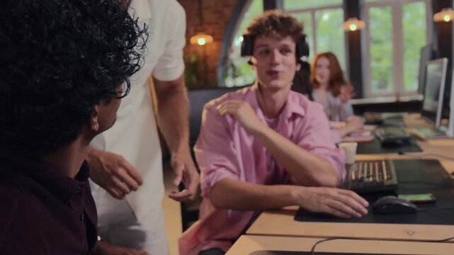 Experienced male manager explaining computer task to young employees in open office. Concept of staff training, workplace mentorship, technical support.