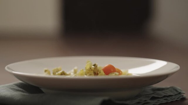 Slow motion making pesto penne pasta with mozzarella and tomatoes in deep plate closeup