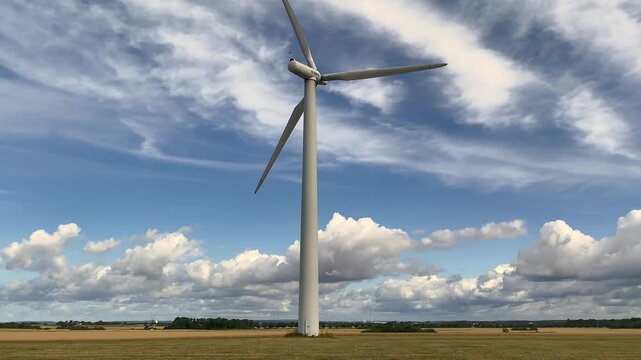 Wind turbine flyby over open field under blue cloudy sky