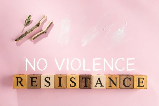 Wooden blocks spelling resistance and no violence text on pink background for social activism and peaceful protest concepts