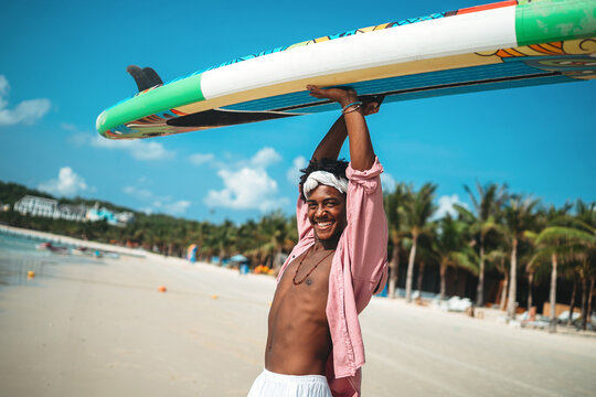 Smiling happy young black man enjoys a sunny day paddling, surf on a tropical beach resort