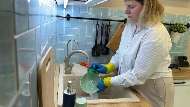 Woman in rubber gloves washing ceramic bowl under water tap in kitchen sink