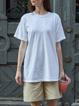 Woman in white t-shirt and beige shorts holding a pink drink outdoors