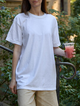 Woman in a white t-shirt holding a pink drink outdoors