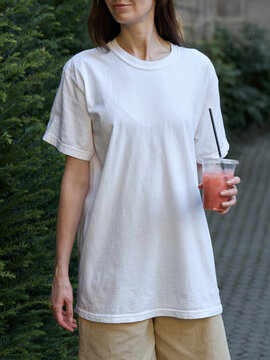 Woman in a white t-shirt and beige shorts holding a refreshing pink drink