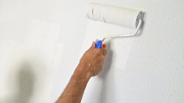hand using paint roller to apply white paint on wall during interior finishing and home renovation process