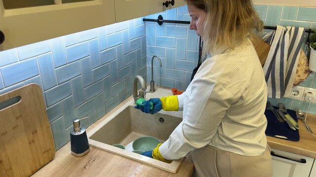 Housewife doing domestic chores cleaning bowls and plates at home standing by wooden countertop with blue tiled wall background