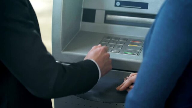Female bank employee showing new client how to work with ATM machine for good service and customer support in 4K Ultra HD footage
