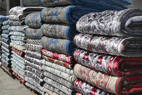 Traditional Uzbek kurpacha mattresses stacked together, showcasing colorful ornamental fabrics and quilted craftsmanship. Authentic Central Asian textile suitable for home decor, hospitality and cultu