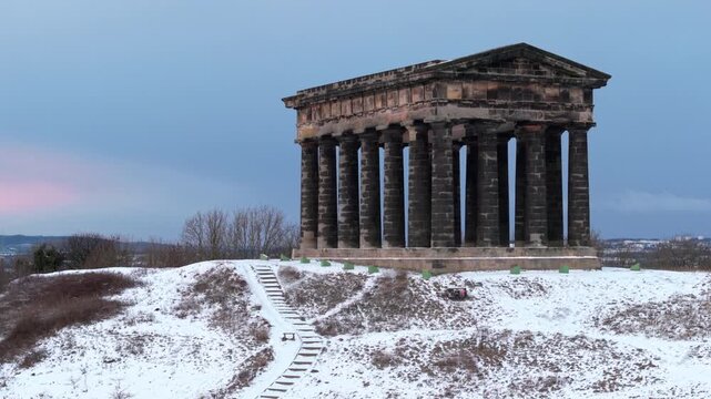Aerial drone shot rising directly in front of the snow-dusted Penshaw Monument in Sunderland, revealing the town of Washington and surrounding winter landscape.