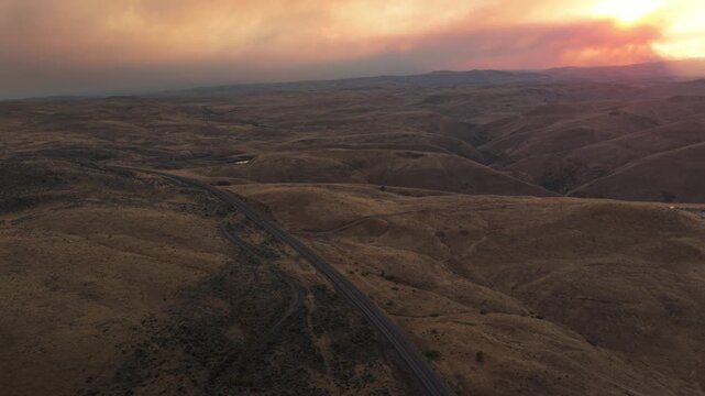 Wide aerial of rolling hills and road at sunset in Midvale Idaho with wildfire smoke from eastern Oregon