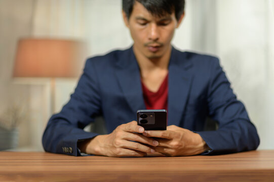 Young Man in a Blue Suit Using a Smartphone at a Wooden Table in Modern Living Room