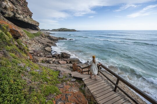Young pretty woman wearing dress off coast and sea at Robberg Nature Reserve, Plettenberg Bay, South Africa