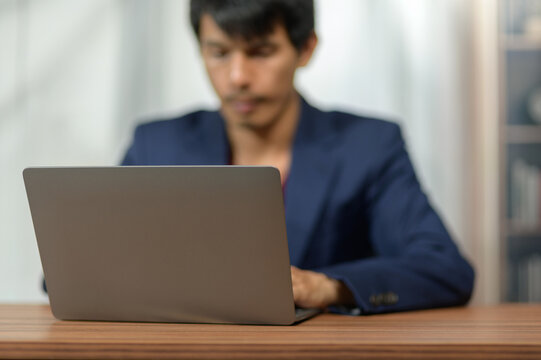Businessman Working on Laptop at Office Desk with Bookshelves in Background