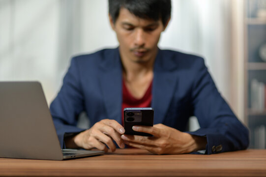 Young Man Working on Smartphone at Desk with Laptop in Modern Office Setting
