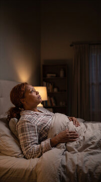 Afro American woman lying awake in bed and staring at the ceiling at night. Insomnia and sleep deprivation concept in vertical format