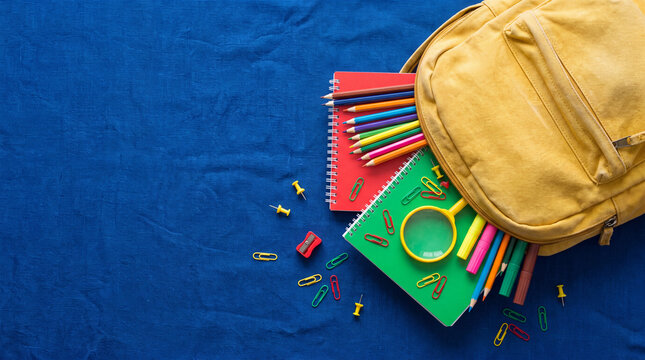 Yellow backpack with colorful notebooks, pencils, and school supplies on a blue background.