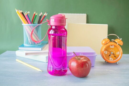 School supplies and healthy lunch on the table for studying. Alarm clock, textbooks, colored pencils and bottle of water and lunch box, back to school concept.
