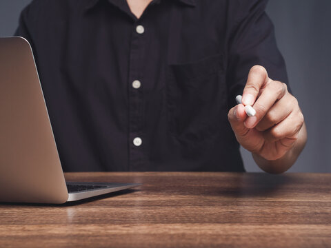 Person writing with stylus beside laptop at office desk