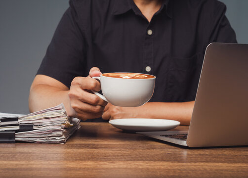 Person holding coffee cup beside laptop at work desk