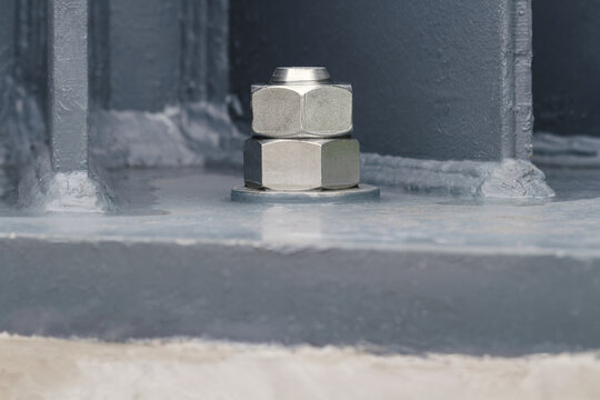 close-up of high-strength steel anchor bolts and heavy hex nuts fastening structural steel column to concrete foundation, steel construction, structural engineering, infrastructure, building assembly