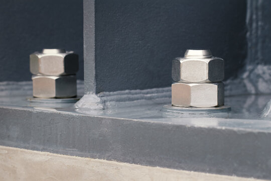 close-up of high-strength steel anchor bolts and heavy hex nuts fastening structural steel column to concrete foundation, steel construction, structural engineering, infrastructure, building assembly