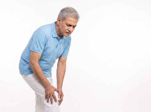 Senior Indian man holding painful knee wearing polo shirt isolated on white background with copy space for arthritis rehabilitation orthopedic healthcare and senior wellness concepts