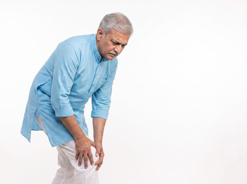 Senior Indian man holding painful knee in traditional kurta isolated on white background with copy space for arthritis rehabilitation orthopedic healthcare and senior wellness concepts