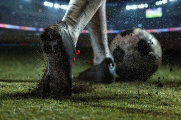 Fototapeta premium Macro view of mud-caked football studs digging into wet turf beside spinning soccer ball. Concept of traction and grip, rainy match action, durable footwear advertising.