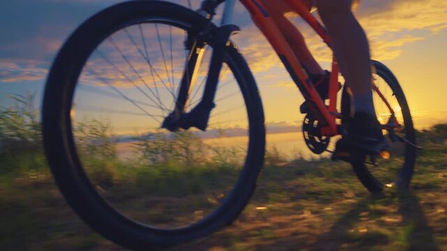 A senior adult engages in an active lifestyle through recreational cycling, pedaling an orange bike against a stunning sunset backdrop.