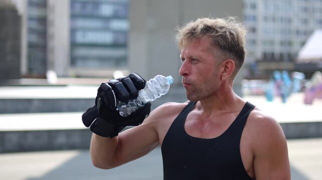 Close-up footage of a middle-aged man takes a breather on his skates, holding a hockey stick as he drinks from a water bottle, showcasing his satisfaction.