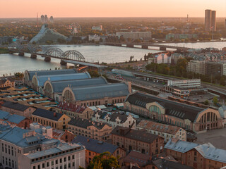 Aerial drone view of the five vaulted pavilions of Riga Central Market, built from former zeppelin hangars, beside the railway bridge and the Daugava river, at sunset. Riga, Latvia. © Aerial Film Studio