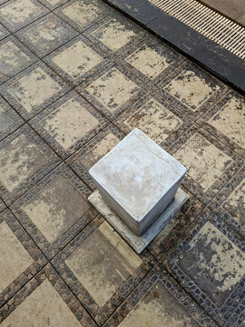 A high-angle view of textured outdoor floor tiles with a square stone block placed on top.
