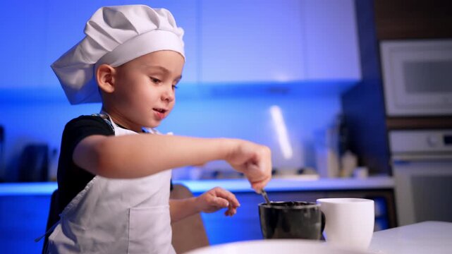 Boy stirring contents of black mug. Viewed in profile, the child reaches toward the mug beside a plain white cup on the table.