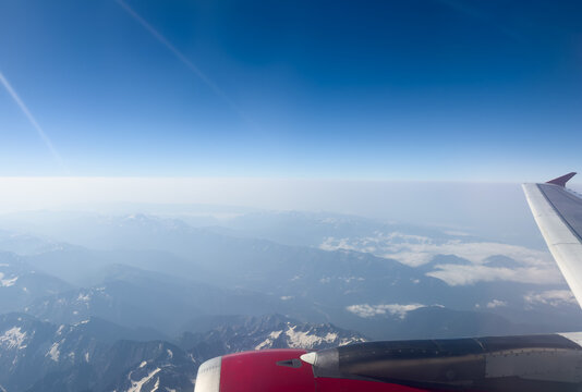 Airplane  wing with mountain range below on sunny day. Great views of desert landscape and snowed peaks from plane