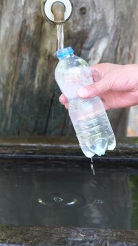 Frisches Trinkwasser aus dem Brunnen in eine leere Flasche abf&uuml;llen um den Durst unterwegs in der Natur zu stillen.