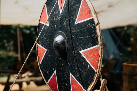 A shield with a unique pattern leans against a display during a medieval festival. The scene highlights elements of historical reconstruction and everyday life from the Middle Ages