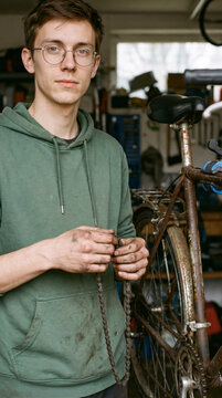 Focused amateur mechanic holding greasy chain beside vintage bicycle in home garage