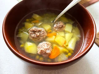 A Ceramic Bowl of Soup with Meatballs, Green Peas and other Vegetables on White Tablecloth. Traditional Slavic Dish. Homemade Food. © troyka