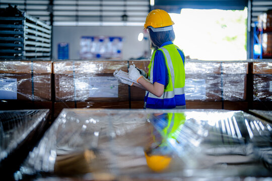 Bearded male warehouse worker and young female colleague in hard hats and safety vests check labels on shrink wrapped export crates in a bright modern distribution warehouse with tall.