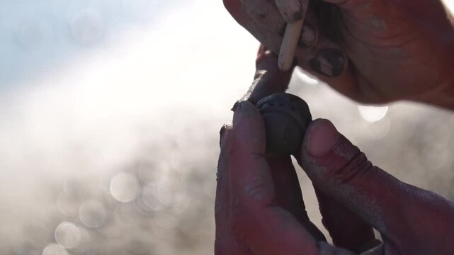 Clay crafting hands shaping small object outdoors, detailing with tools in bright sunlight, artistic pottery work
